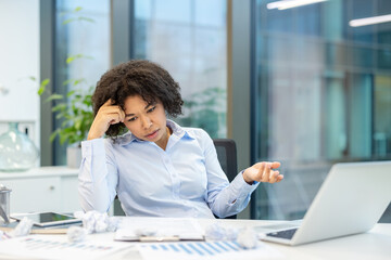 Obraz premium Tired and worried young African American woman sitting at the desk in the office and looking disappointedly at the crumpled paper