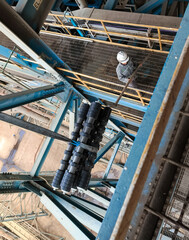 Industrial lifting operation of conveyor rollers using a crane at a power plant or factory.