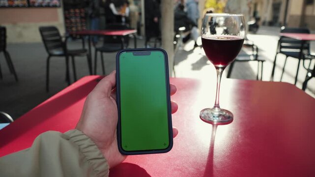 Man using a smartphone with a chroma key green screen and drinking red wine on the terrace of cafe, selects dishes from the restaurant menu using a QR code. High quality 4k footage
