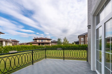 The scene shows a balcony with a view of multiple houses and a large green lawn. The sky has clouds and is bright with sunlight. It is a peaceful day in the suburbs © Alhim