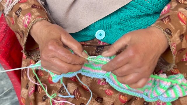 Lady with wrinkly hands knitting in free time. Old lady knitting colorful sweater. Elderly female knitting from wool with needles. Knitting sweater with wrinkly hands. Colorful Crochet with old hands.