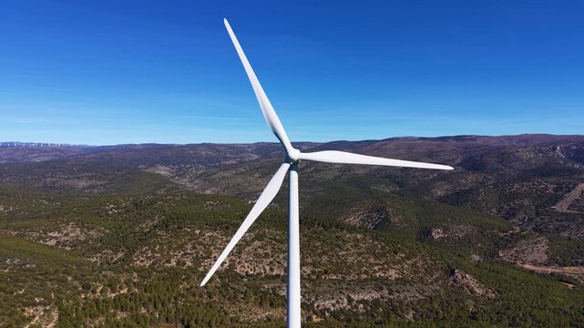 Aerial close-up of a utility-scale wind turbine with rotor, nacelle and tower above rugged mountain terrain, showing renewable power infrastructure in operation