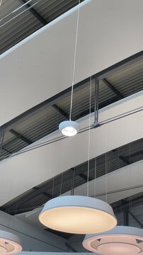 Circular ring lights suspended in modern atrium, closeup of flat disc and halo fixtures beneath exposed beams. Warm LED glow contrasts with cool metal