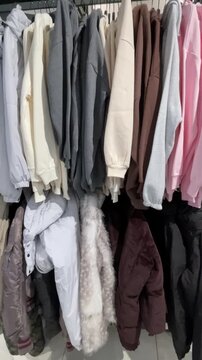 Assorted coats on store rack shelves with pink brown beige rows, fur trims and padded silhouettes visible in layered outerwear display