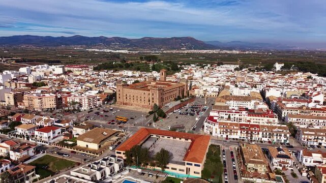 Orbit aerial panorama of El Puig de Santa Maria showing the historic monastery, dense residential blocks and Valencian countryside backed by mountains
