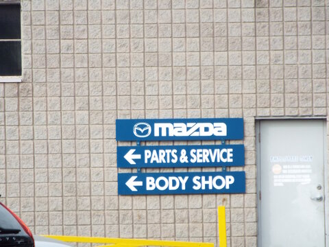 Ottawa, Ontario, Canada-July 22, 2025: Blue directional signs for "Mazda Parts and Service and Body Shop" are mounted on a tan stone block wall on Carling Avenue.