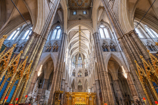 People visit Westminster Abbey in London to explore its historic architecture. Sunlight shines through stained glass windows, illuminating the high arches and detailed design inside.