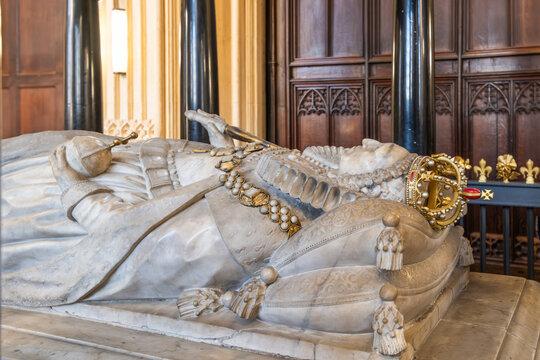 The tomb of Elizabeth I is in Westminster Abbey in London, UK. The stone monument shows the figure of the queen with a crown and regal attire. Visitors observe and reflect on the history.
