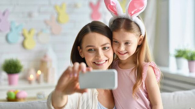 Smiling mother and daughter taking Easter selfie at home, bunny ears headband, cozy spring holiday celebration, pastel room decor, joyful childhood memory, tender family bonding moment