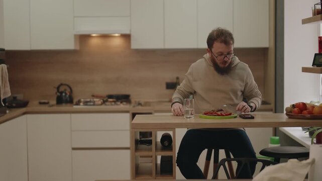 Bearded Man Enjoying a Healthy Meal and Checking His Smartphone in a Modern Kitchen