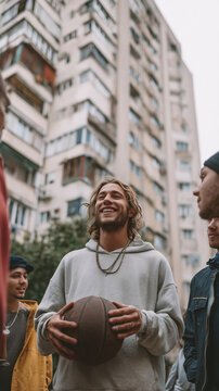 Young man smiling, holding basketball, talking with friends in urban setting, enjoying streetball community