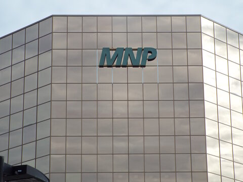 Ottawa, Ontario, Canada-July 22, 2025: A green "MNP" logo is mounted on the mirrored glass facade of a modern multi-story commercial office building at 1600 Carling Ave Suite 800.