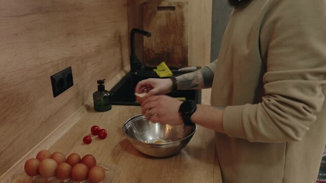 Preparing a Healthy Breakfast: Person Cracks Fresh Eggs into a Bowl in a Modern Kitchen