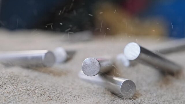 Close up of aluminum rods being gradually covered by loose quartz sand, where their defined shape fades into a more uniform and disordered structure.