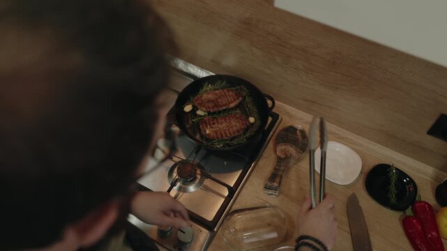 Man Flips Savory Meat with Rosemary and Garlic in a Sizzling Pan on a Gas Stove