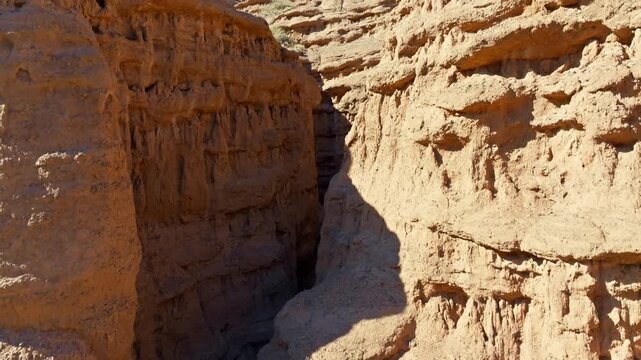Ascending reveal aerial view captures stunning geological formations in arid landscape of Kyrgyzstan. Dramatic canyons and rock formations showcase natural beauty under bright daylight.