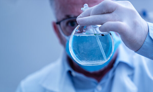 Scientist wearing mask and gloves holding a flask with blue liquid containing microplastics