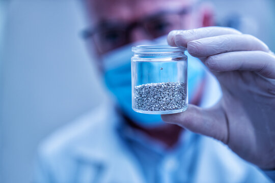 Scientist in lab holding glass vial containing granular rare earth elements