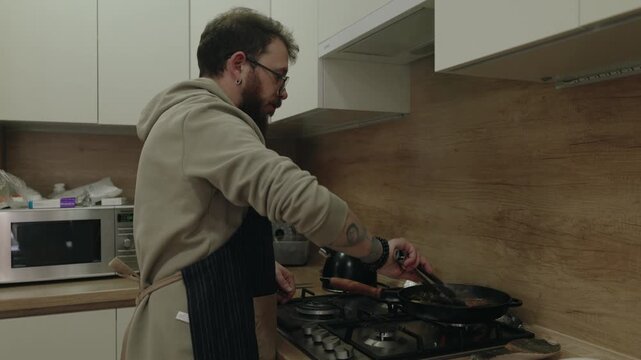 A Man Wearing an Apron Intently Cooks Food in a Modern Kitchen at Home
