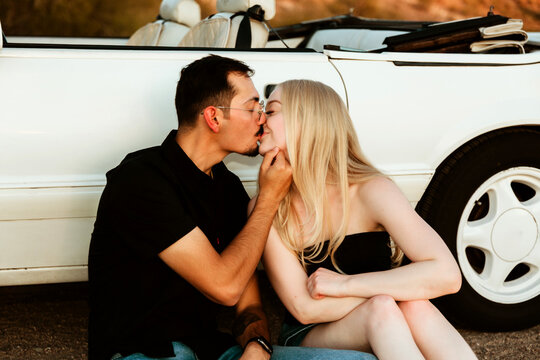 seated couple kissing in the desert by car