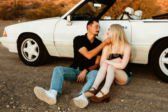 couple sitting by classic car in the dessert showing affection
