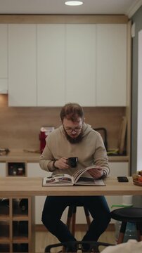 Man With Glasses And Beard Reads A Book While Enjoying Coffee In A Modern Kitchen