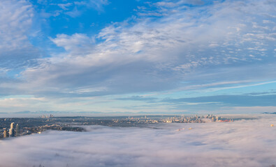 Naklejka premium Aerial Fog Over Vancouver And Burnaby Skyline With Morning Clouds And Distant Mountains, BC