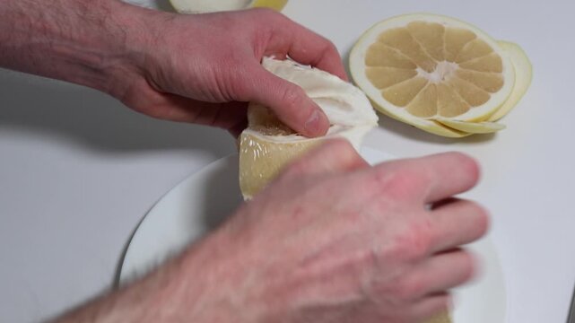Peeling a pomelo fruit to reveal its juicy segments, a top-down view of the process of preparing the citrus fruit for consumption, highlighting the texture and color of the flesh