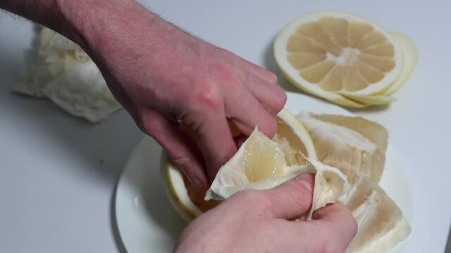Close-up footage displays the careful peeling of a pomelo, removing sections from the pith, demonstrating the preparation of this vibrant, healthy fruit snack, emphasizing fresh ingredients.
