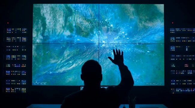 Silhouette of a operator interacting with a large digital map on a tech command center wall screen in a dark control room