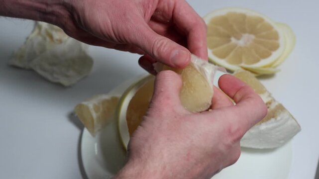 Hands Skillfully Remove White Fibers from Pomelo Wedges, Creating a Refreshing and Healthy Snack, Revealing Vibrant Fruit Segments Arranged on a White Plate, Perfect for Culinary Creations.