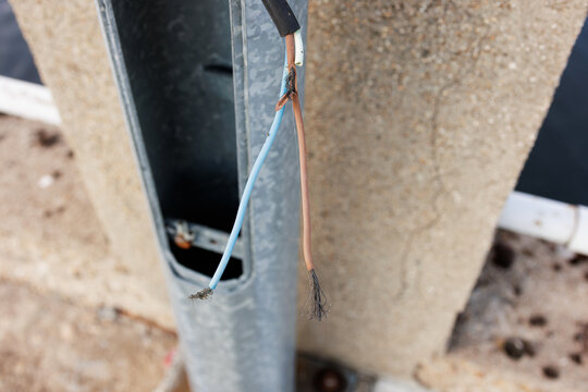 Close-up of exposed power cables protruding from a damaged galvanized steel lamp post on a concrete bridge or walkway. Stock photo