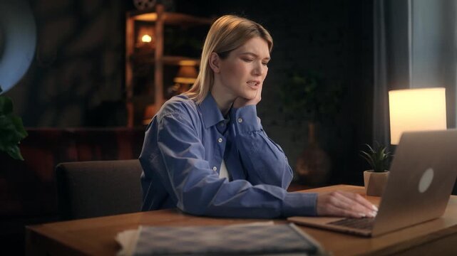 Young woman working on laptop at home office at night suddenly feeling sharp toothache and touching her cheek