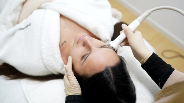 Professional cosmetologist using a radio frequency lifting machine on a woman's face for a rejuvenating and tightening facial treatment in a modern aesthetic medicine clinic