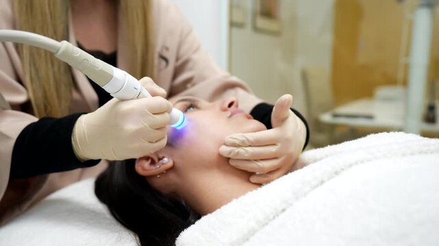 Professional cosmetologist performing a rejuvenating hydrafacial procedure on a female client's cheek with a special device in an aesthetic clinic for a deep cleansing and anti aging effect