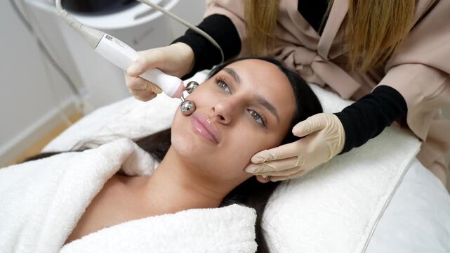 Relaxed young woman receiving a non invasive microcurrent facial treatment from a professional beautician to stimulate muscles, improve skin tone, and reduce wrinkles in a modern spa