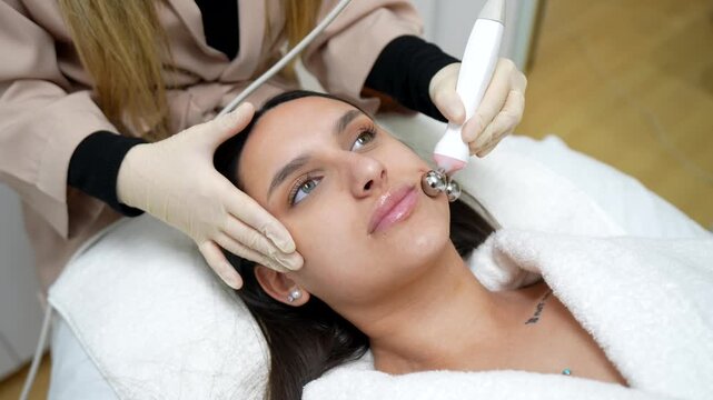 Professional cosmetologist performing a stimulating microcurrent facial therapy on a young woman's skin with an electrical device in a beauty salon for a rejuvenating anti aging lifting effect