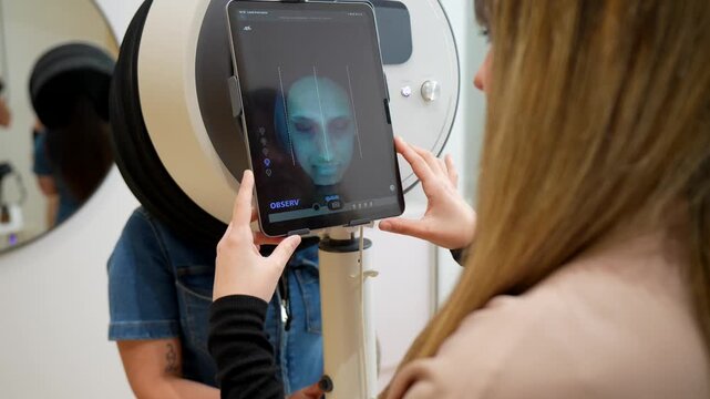 Professional beautician using modern facial scanning technology to perform a deep skin analysis on a client, observing the digital 3d model on a tablet in a beauty clinic