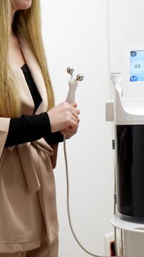 Professional female beautician in a uniform taking a microcurrent wand and setting up the modern cosmetology equipment for a facial treatment session in a contemporary beauty clinic