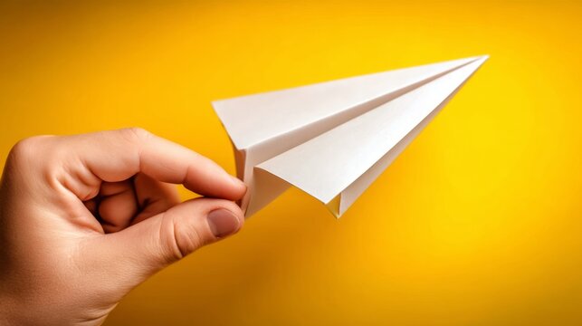 Hand launching paper airplane against bright yellow backdrop