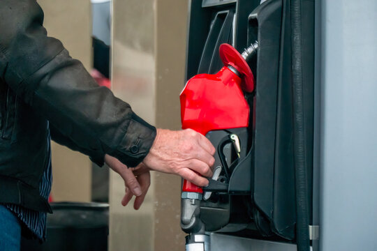 Close-up of a hand reaching for a red gas pump nozzle at a fueling station to refill a vehicle.