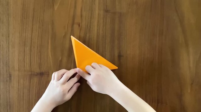 Child hands creasing orange origami paper step by step, slow motion