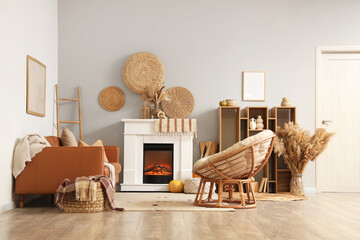 Fototapeta premium Interior of living room with leather sofa, armchair, shelving unit, wicker basket, fireplace and autumn decorations