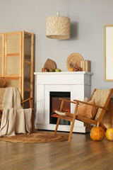 Fototapeta premium Interior of living room with armchairs, closet and autumn decorations on fireplace