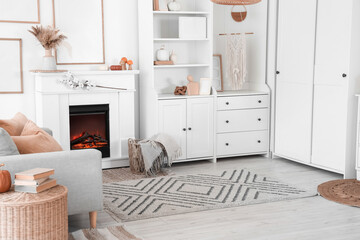 Fototapeta premium Interior of living room with grey sofa, coffee table, shelving units and autumn home decor on fireplace near white wall