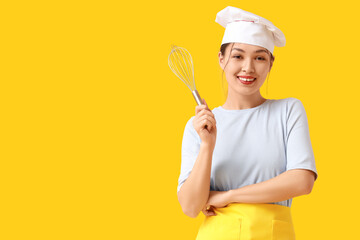 Naklejka premium Beautiful young happy Asian woman with whisk on yellow background