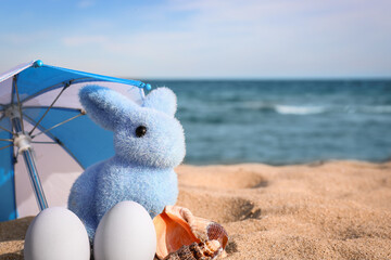 Fluffy toy bunny, umbrella and painted Easter eggs on sea beach
