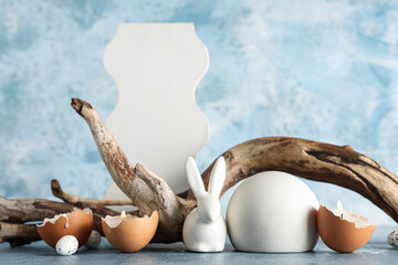 Decorative podiums with toy bunny, burning candles and tree branch on blue background