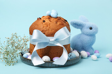 Plate with delicious Easter cake, painted eggs and bunny on blue background
