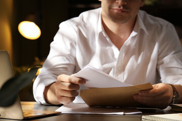 Fototapeta premium Man putting letter into envelope at wooden table indoors, closeup